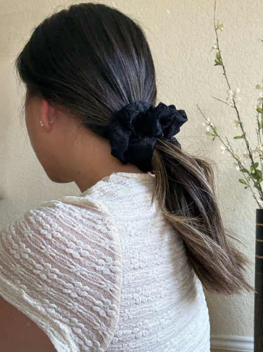 Person with a ponytail wearing a black scrunchie, wearing a textured white top.