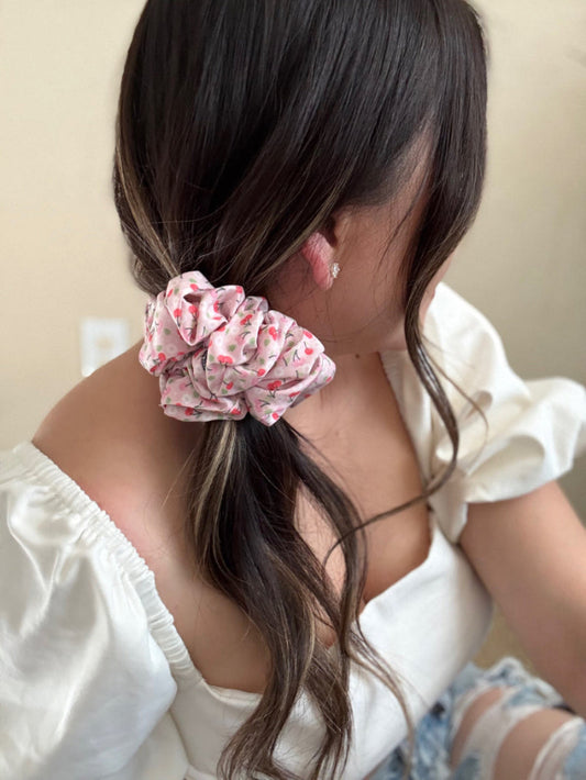Person with a pink scrunchie in their hair against a neutral background