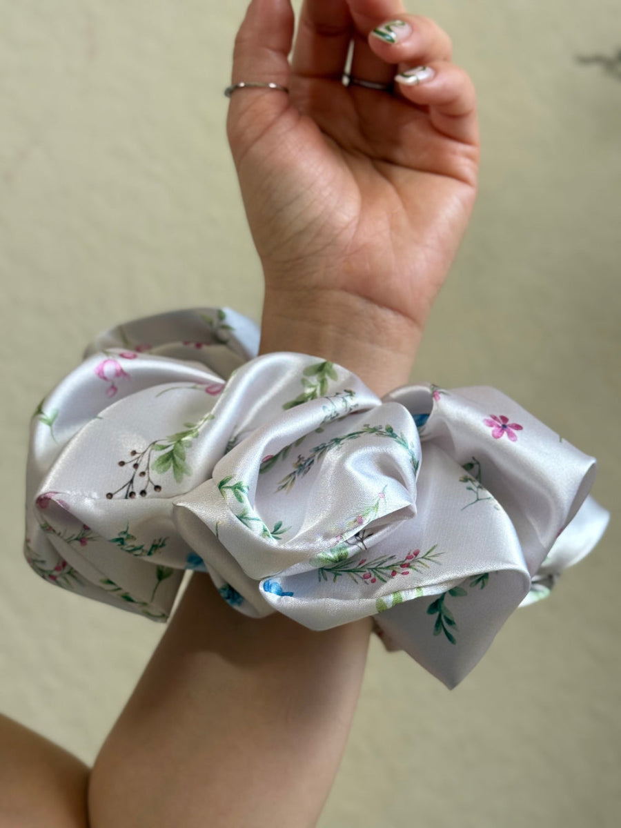 Ivory satin floral scrunchie with soft blue, pink, and green flowers on a neutral base, designed for thick and long hair, offering a secure and stylish hold.