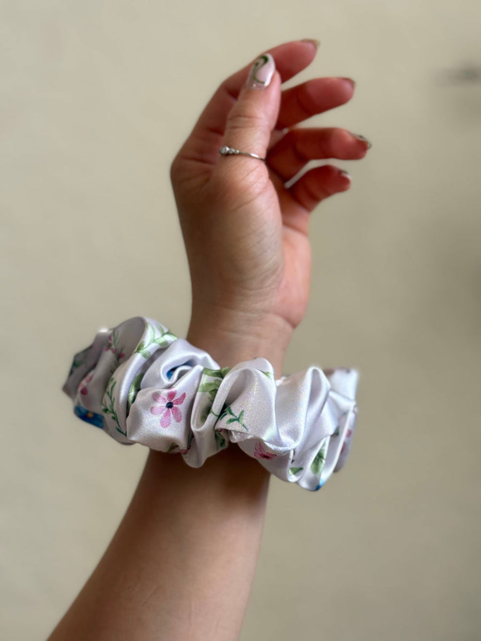 A midi satin floral scrunchie with a delicate pattern in blue, pink, and green on a white background.