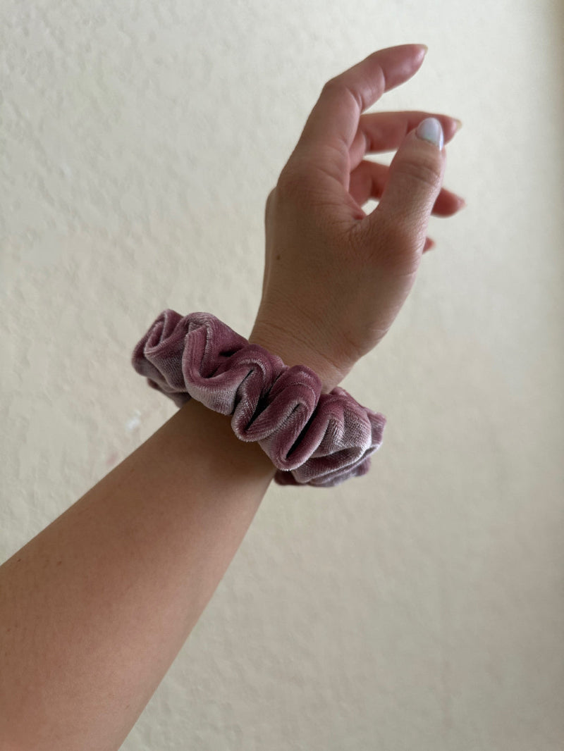 Hand wearing a pink scrunchie on a plain background