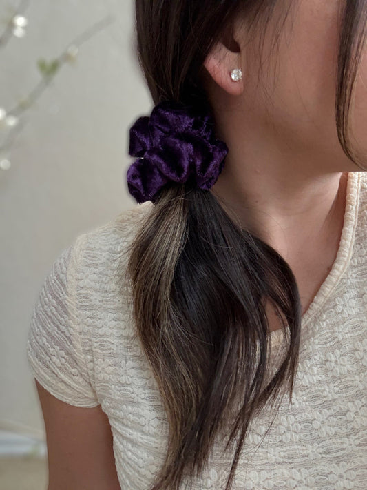 Close-up of a person with a purple scrunchie in their hair, wearing a light-colored top.