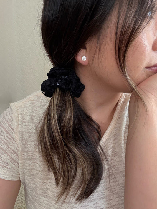 Close-up of a person with a black scrunchie in their hair, wearing a beige top.