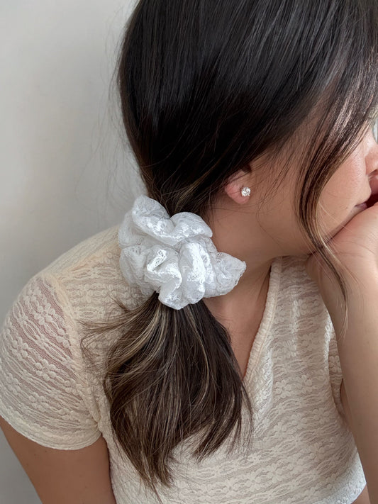 Woman with a white scrunchie in her hair wearing a beige top against a neutral background