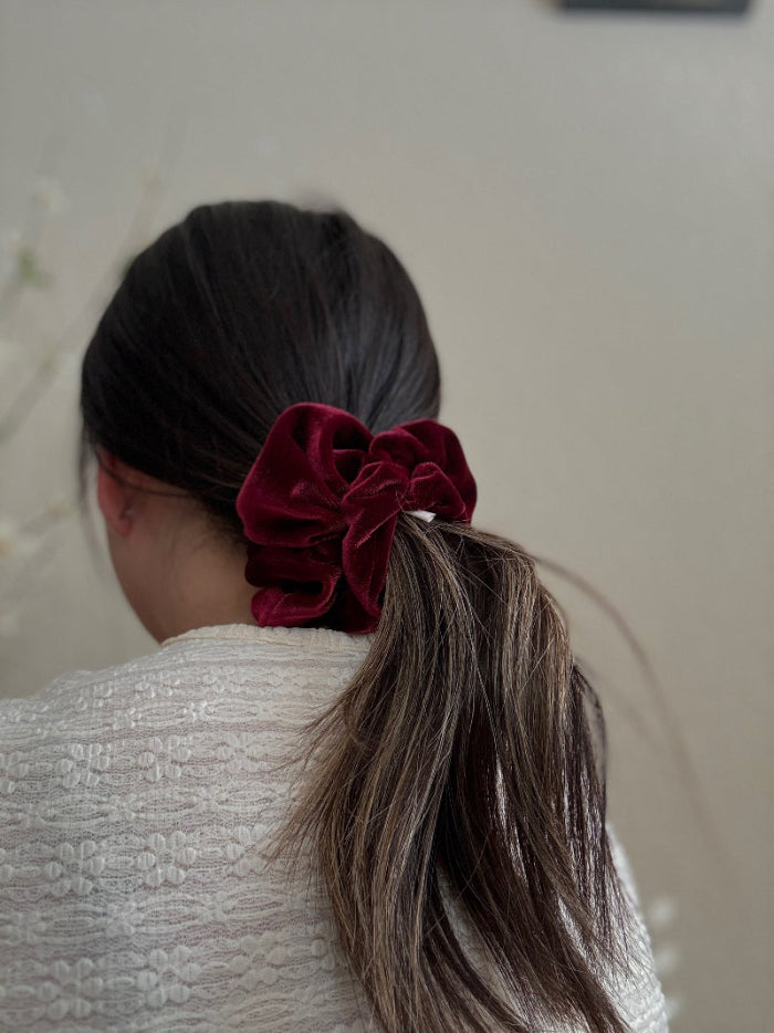 Person with a red scrunchie in their hair against a neutral background
