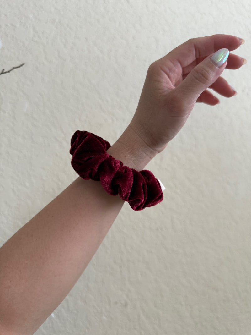 Hand wearing a burgundy scrunchie on a plain background