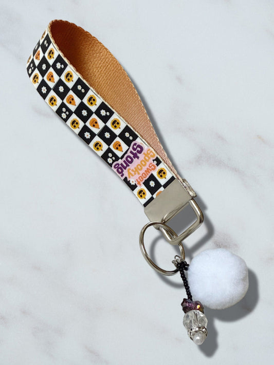 Keychain with checkered strap, white ball, and decorative elements on a light gray background