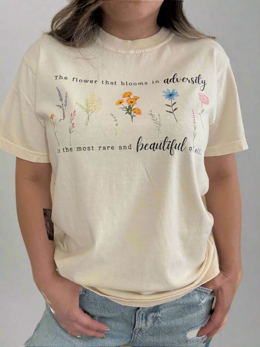 Person wearing a beige t-shirt with floral designs and text on a plain background