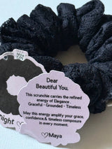 Black scrunchie with a tag featuring text and branding on a light blue background