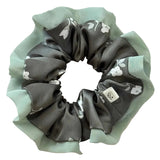 Two scrunchies, one gray with white floral patterns and one green, on a light beige background.