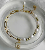 A gold and white beaded bracelet with a crescent moon and sun charm, displayed on a clear glass dish.