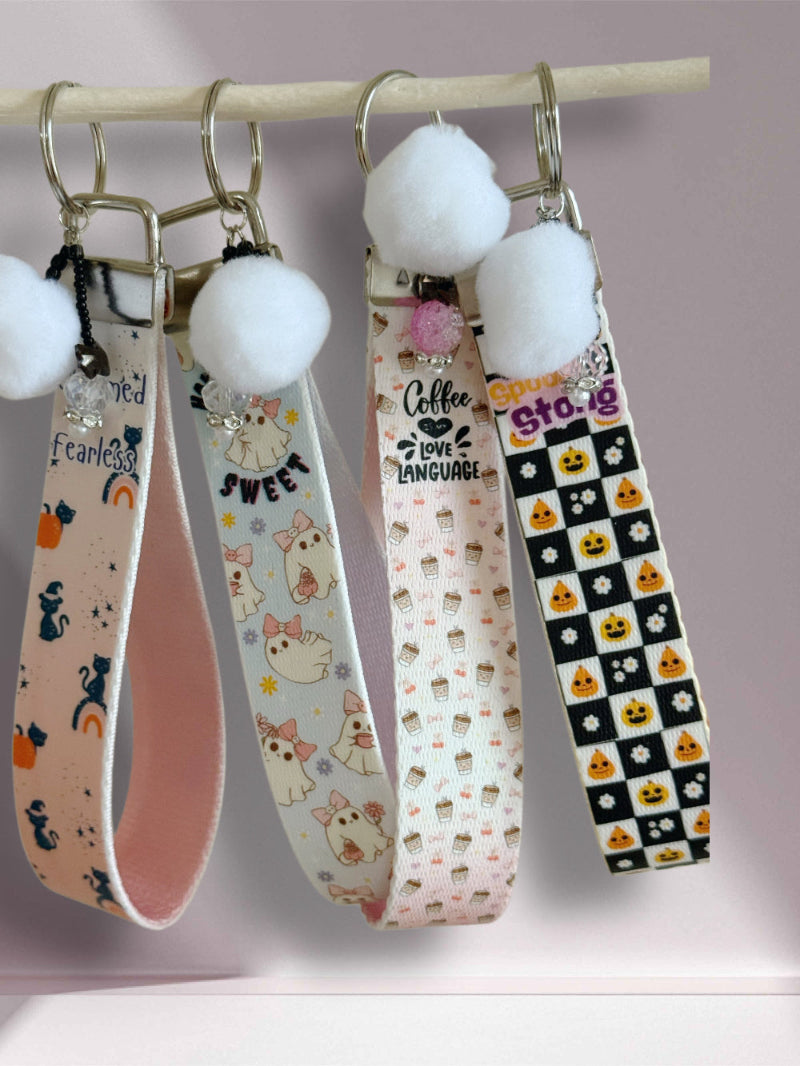 Four keychains with different designs hanging on a rod against a light purple background.