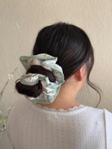 Person with a floral scrunchie in their hair against a neutral background