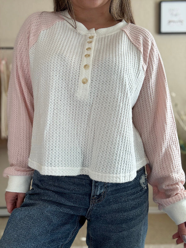A woman wearing a color block henley top in pink and ivory with a classic Henley neckline and button details.