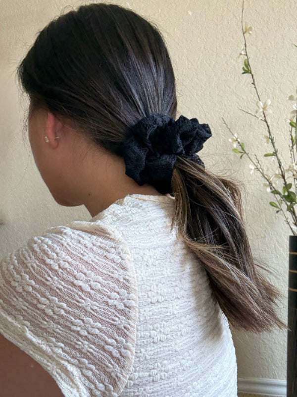 Person with a ponytail wearing a black scrunchie, wearing a textured white top.