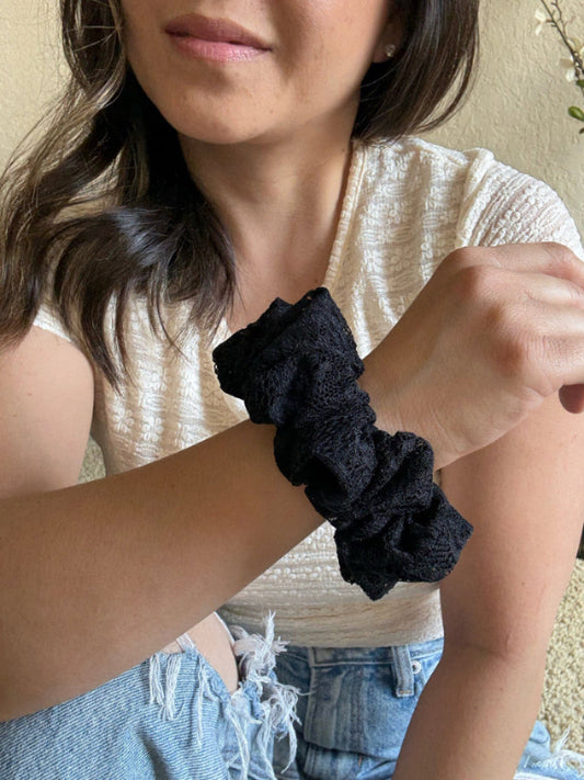 Person wearing a black scrunchie on their wrist with a neutral background