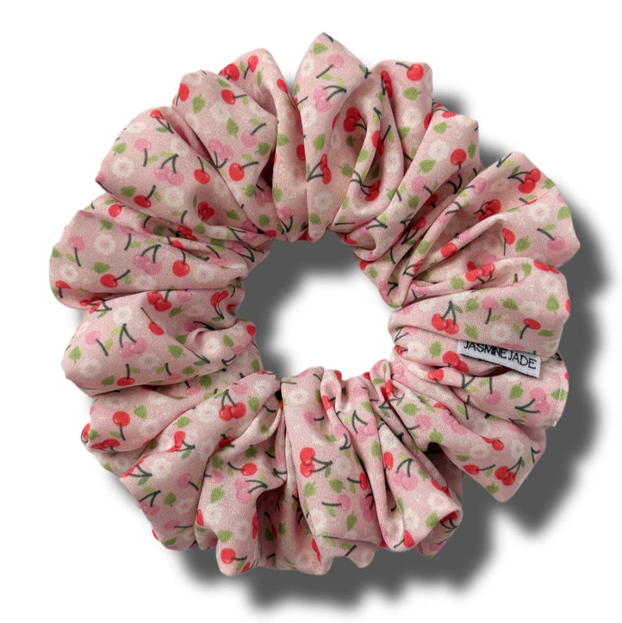 Pink scrunchie with cherry pattern on a white background
