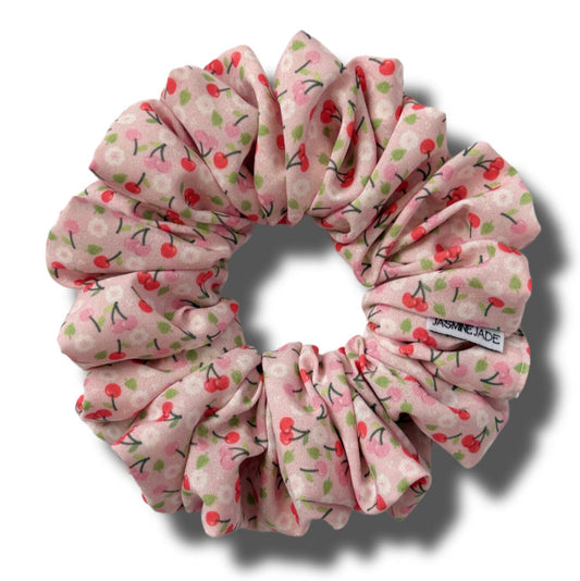 Pink scrunchie with cherry pattern on a white background