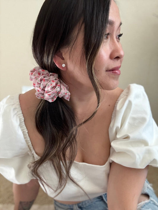 Woman wearing a floral scrunchie in her hair against a neutral background
