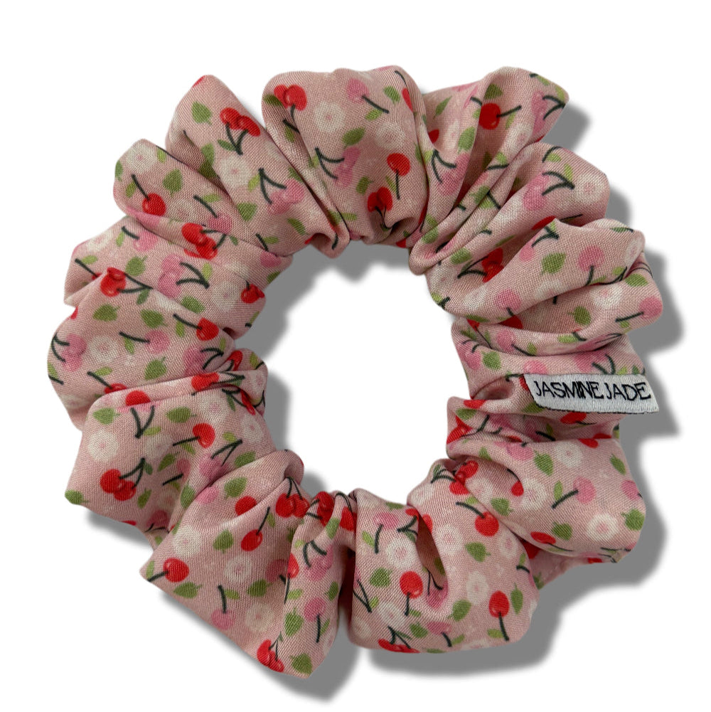 Pink scrunchie with cherry pattern on a white background