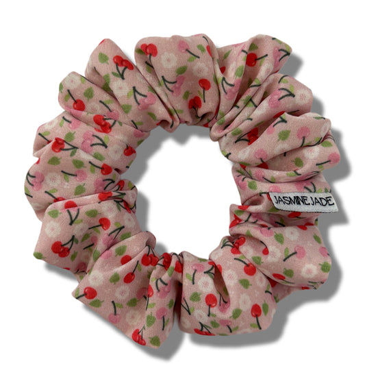 Pink scrunchie with cherry pattern on a white background