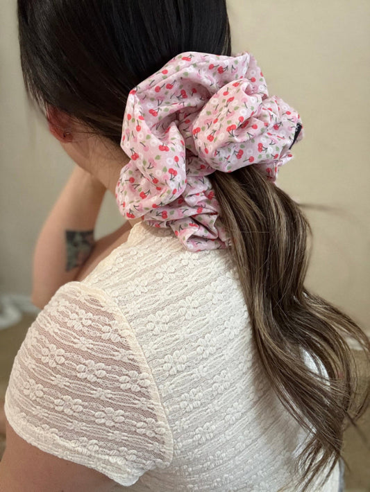 Person wearing a floral scrunchie in their hair with a neutral background