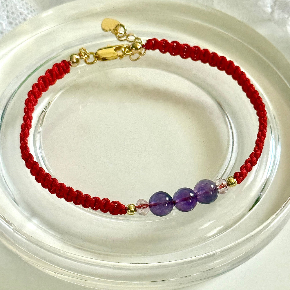 Bracelet with red cord and purple beads on a clear stand