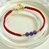 Bracelet with red cord and purple beads on a clear stand