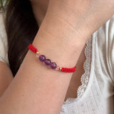 Close-up of a wrist wearing a red beaded bracelet with purple beads.