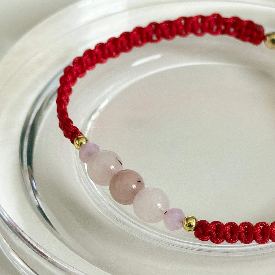 Red string bracelet with pink beads on a clear glass surface
