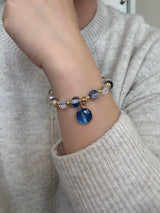 Bracelet with blue and gold beads on a wrist, wearing a light gray sweater.