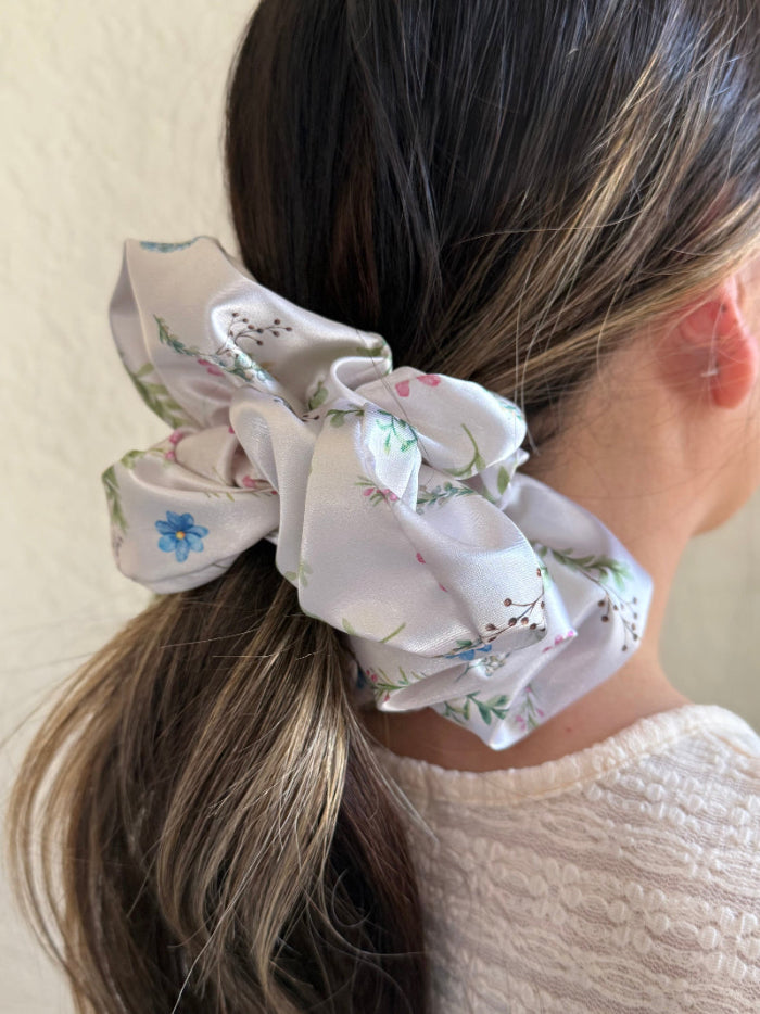 Ivory satin floral scrunchie with soft blue, pink, and green flowers on a neutral base, designed for thick and long hair, offering a secure and stylish hold.
