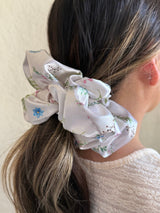 Ivory satin floral scrunchie with soft blue, pink, and green flowers on a neutral base, designed for thick and long hair, offering a secure and stylish hold.
