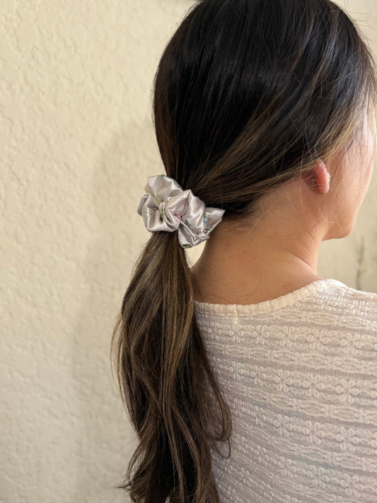 Person with a ponytail wearing a silver scrunchie against a neutral background