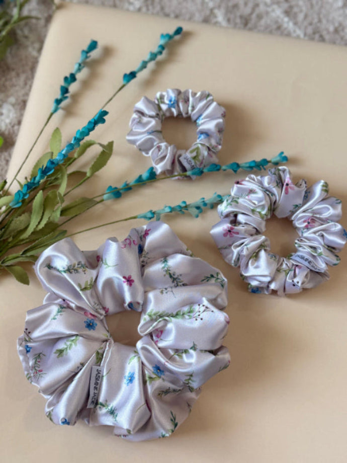 ivory satin floral scrunchie with delicate blue, pink, and green flowers on a neutral base, designed for every day wear, offering a secure and stylish hold.