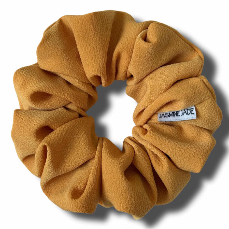 Mustard yellow scrunchie with a brand label on a white background