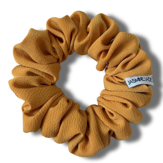 Mustard yellow scrunchie with a visible brand label on a white background