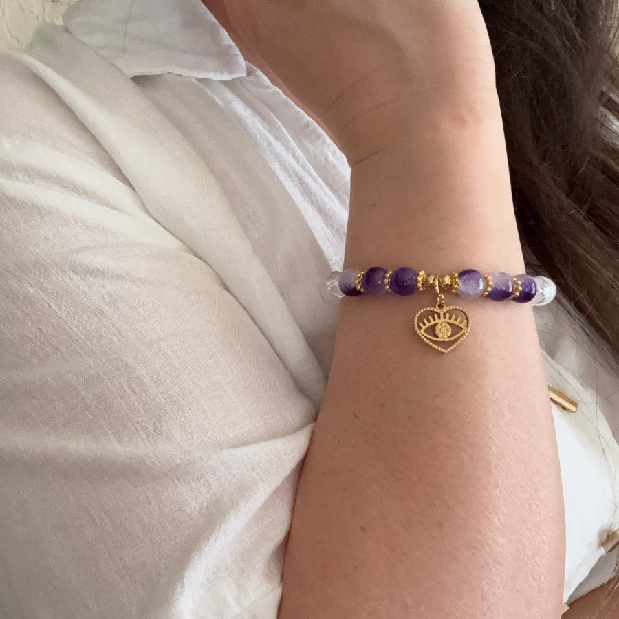 Close-up of a wrist wearing a bracelet with purple beads and a gold charm.