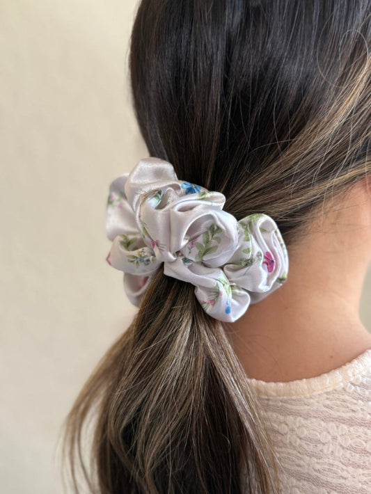 Model wearing a  midi satin floral scrunchie with a delicate pattern in blue, pink, and green on a white background.