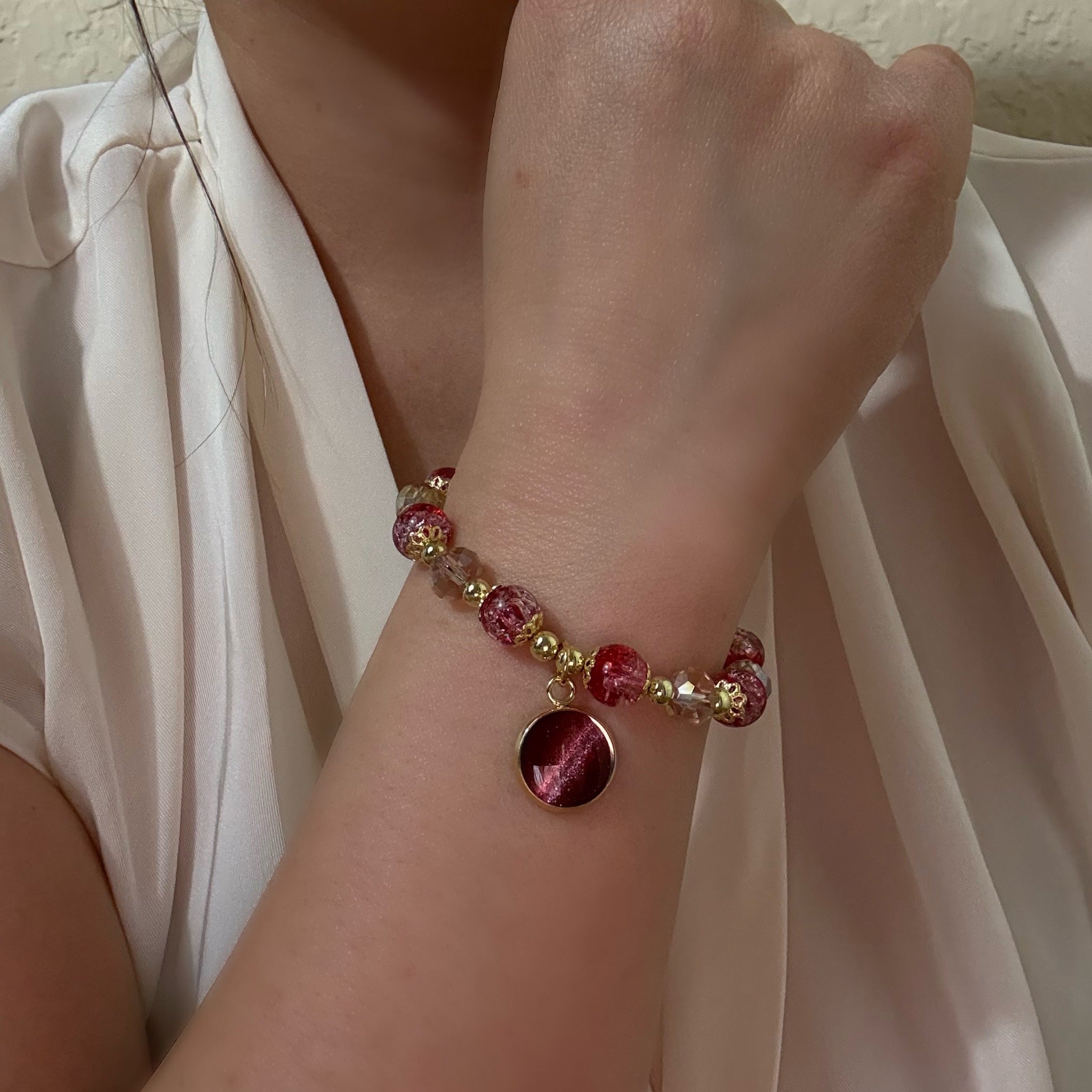 Bracelet with red and gold beads on a wrist against a neutral background