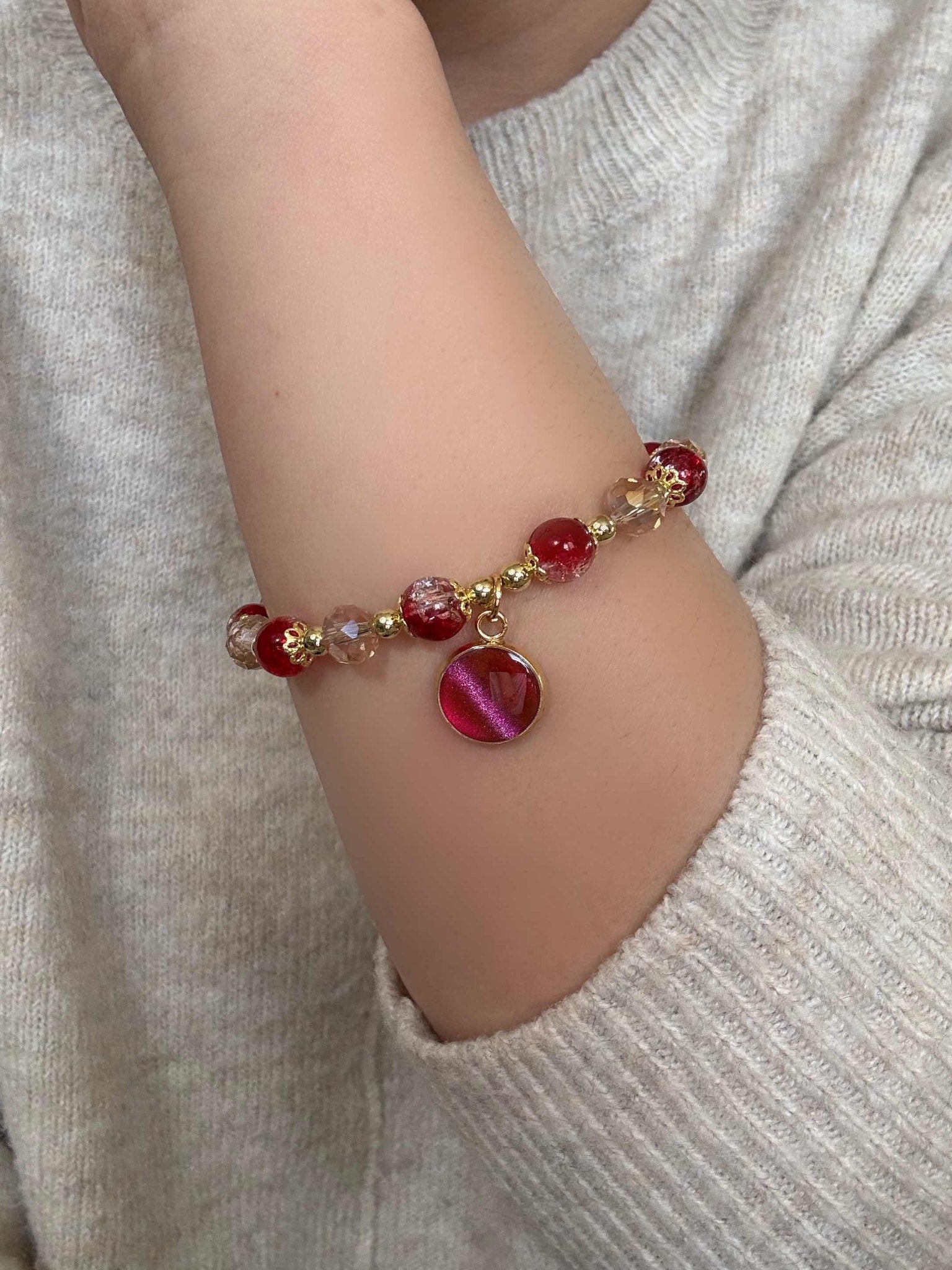 Bracelet with red beads and a heart charm on a wrist against a neutral background