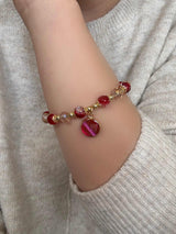 Bracelet with red beads and a heart charm on a wrist against a neutral background