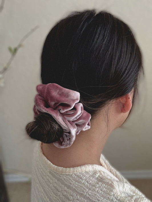 Person wearing a pink scrunchie in their hair against a neutral background