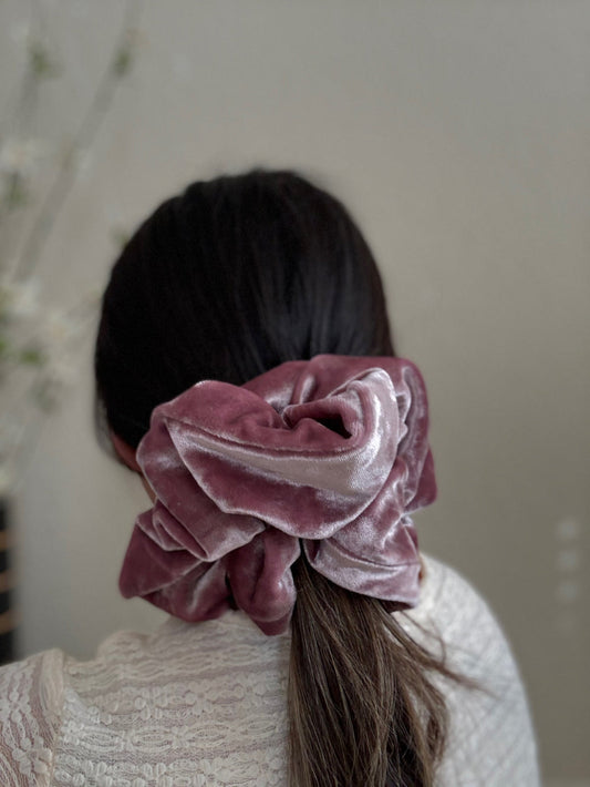 Person wearing a pink velvet scrunchie in their hair against a neutral background