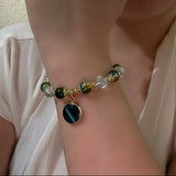 Close-up of a wrist wearing a bracelet with colorful beads and a dark green pendant.