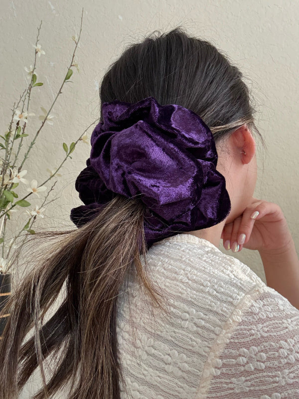 Person wearing a purple scrunchie in their hair against a neutral background