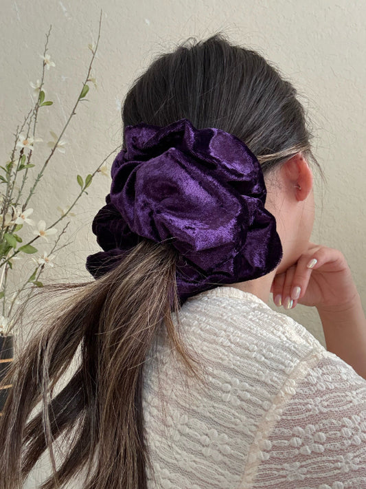 Person wearing a purple scrunchie in their hair against a neutral background