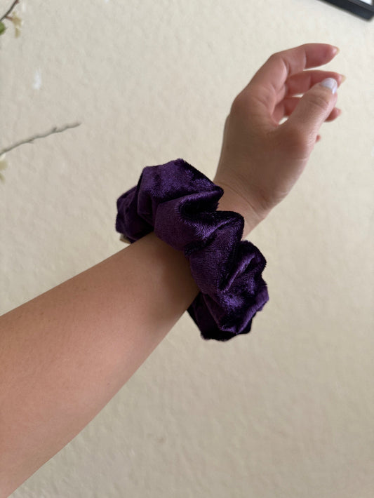 Purple scrunchie on a wrist against a plain background