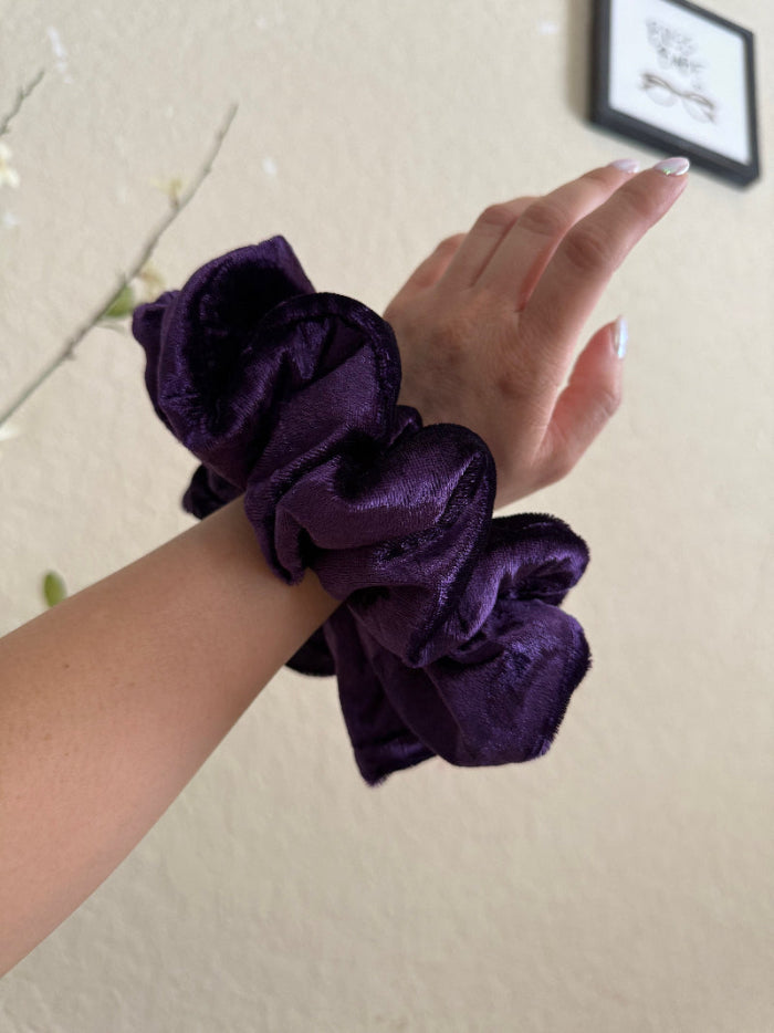 Purple scrunchies on a wrist with a neutral background