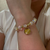Bracelet with clear beads and a gold charm on a wrist against a neutral background